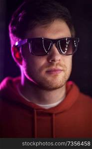 leisure, clubbing and nightlife concept - portrait of smiling young man in sunglasses at dark room over ultra violet neon lights of night club. man in sunglasses over ultra violet neon lights