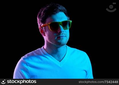 leisure, clubbing and nightlife concept - portrait of young man in sunglasses at dark room over ultra violet neon lights. man in sunglasses over ultra violet neon lights