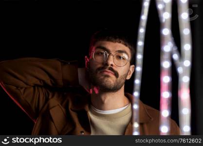 leisure, clubbing and nightlife concept - young man in glasses ain dark room over ultra violet neon lights at night club. man in glasses over neon lights at nightclub