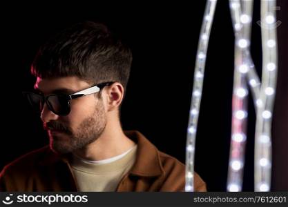 leisure, clubbing and nightlife concept - young man in sunglasses ain dark room over ultra violet neon lights at night club. man in sunglasses over neon lights at nightclub