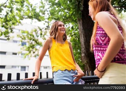 leisure, communication and friendship concept - happy smiling teenage girls or friends talking on city street in summer. teenage girls or friends talking in summer city