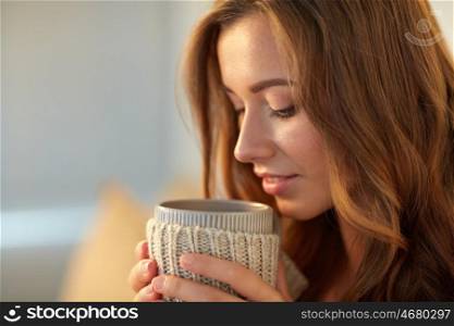 leisure, drink, winter and people concept - close up of happy young woman with cup of coffee or tea at home