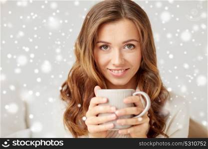 leisure, drink, winter and people concept - close up of happy young woman with cup of coffee or tea at home over snow. close up of happy woman with coffee cup at home