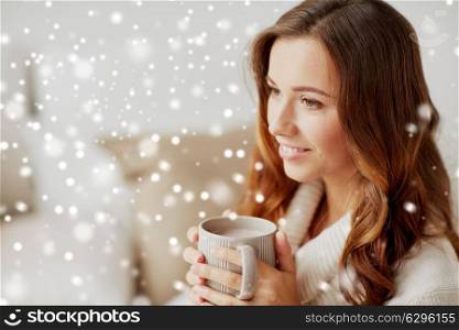 leisure, drink, winter and people concept - happy young woman with cup of coffee or cocoa at home over snow. happy woman with cup of cocoa or coffee at home
