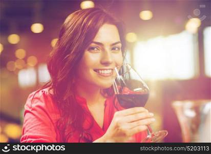 leisure, drinks, degustation, people and holidays concept - smiling woman drinking red wine at restaurant. smiling woman drinking red wine at restaurant