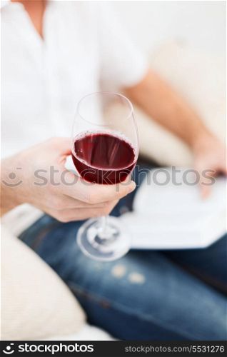 leisure, drinks, education and lifestyle concept - close up of male hand holdind book and glass of red wine