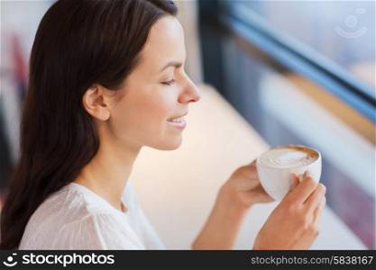 leisure, drinks, people and lifestyle concept - close up of smiling young woman drinking coffee at cafe