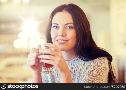 leisure, drinks, people and lifestyle concept - smiling young woman drinking tea at cafe. smiling young woman drinking tea at cafe