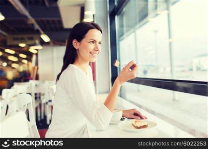 leisure, drinks, people and lifestyle concept - smiling young woman eating cake and drinking coffee at cafe