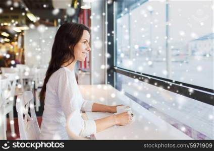 leisure, drinks, people, holidays and lifestyle concept - smiling young woman drinking coffee at cafe over snow effect