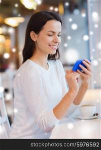 leisure, drinks, people, technology and lifestyle concept - smiling young woman with smartphone drinking coffee at cafe over snow effect