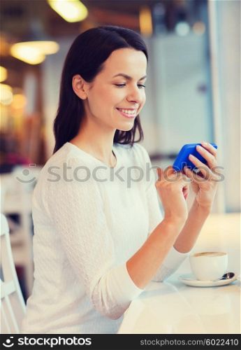 leisure, drinks, people, technology and lifestyle concept - smiling young woman with smartphone drinking coffee at cafe