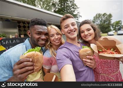 leisure, eating and people concept - happy friends with wok and burgers taking selfie at food truck. happy friends taking selfie at food truck
