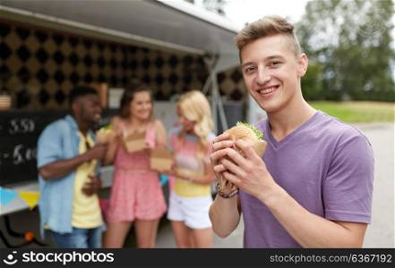 leisure, eating and people concept - happy man with hamburger and friends at food truck. happy man with hamburger and friends at food truck