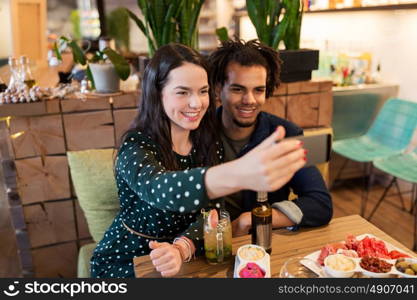 leisure, eating, food and drinks, people and holidays concept - happy couple with drinks at cafe or bar. happy couple taking selfie at cafe or bar
