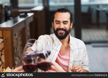 leisure, eating, food and drinks, people and holidays concept - happy man with friends clinking glasses of wine at restaurant