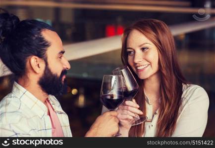 leisure, eating, food and drinks, people and holidays concept - smiling couple celebrating anniversary and clinking red wine glasses at restaurant. couple drinking red wine and clinking glasses