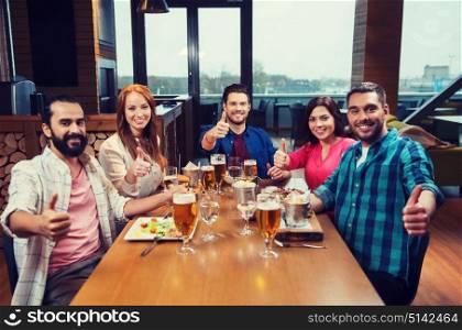 leisure, eating, food and drinks, people and holidays concept - smiling friends having dinner and drinking beer and showing thumbs up at restaurant or pub. friends dining and drinking beer at restaurant