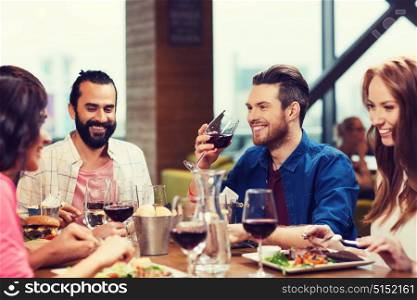 leisure, eating, food and drinks, people and holidays concept - smiling friends having dinner and drinking red wine at restaurant. friends dining and drinking wine at restaurant