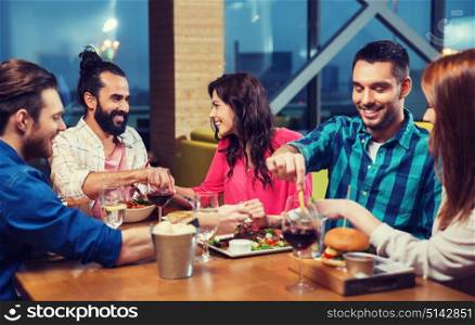 leisure, eating, food, people and holidays concept - smiling friends having dinner and tasting each other dish at restaurant. friends eating and tasting food at restaurant