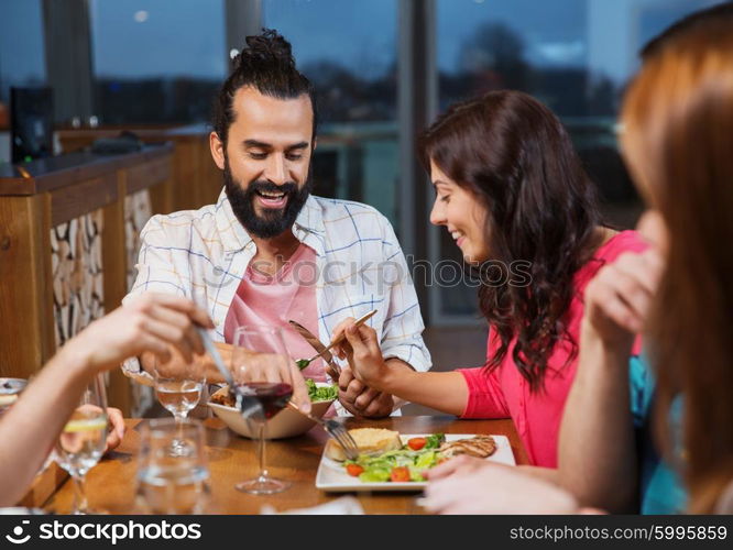 leisure, eating, food, people and holidays concept - smiling friends having dinner and tasting each other dish at restaurant