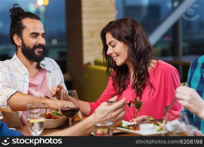 leisure, eating, food, people and holidays concept - smiling friends having dinner and tasting each other dish at restaurant