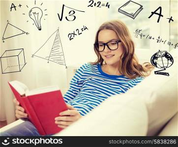 leisure, education and home concept - smiling teenage girl in glasses reading book and sitting on couch at home