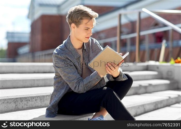 leisure, education and people concept - young man or teenage boy with notebook, diary or sketchbook writing or drawing in city. young man with notebook or sketchbook in city