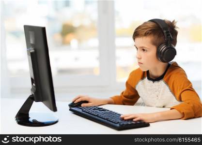 leisure, education, children, technology and people concept - boy with computer and headphones typing on keyboard or playing video game at home