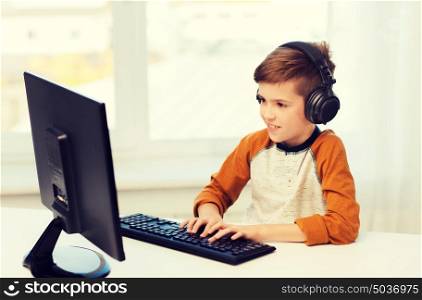 leisure, education, children, technology and people concept - happy boy with computer and headphones typing on keyboard or playing video game at home. happy boy with computer and headphones at home