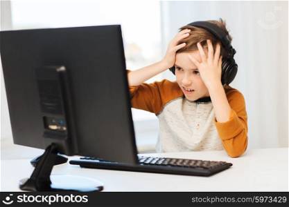 leisure, education, children, technology and people concept - terrified boy with computer and headphones playing video game at home