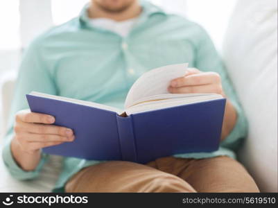 leisure, education, literature and home concept - close up of man and sitting or lying on couch and reading book at home