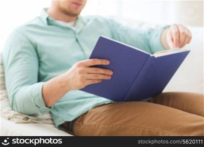 leisure, education, literature and home concept - close up of man and sitting or lying on couch and reading book at home