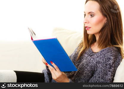 Leisure, education, literature and home concept - Woman sitting on couch reading book at home