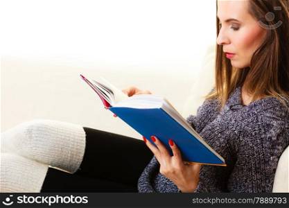 Leisure, education, literature and home concept - Woman sitting on couch reading book at home