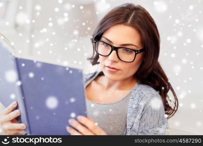 leisure, education, vision, winter and people concept - young woman in glasses reading book at home over snow