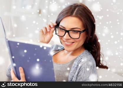 leisure, education, vision, winter and people concept - young woman in glasses reading book at home over snow