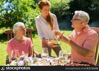 leisure, family and people concept - happy daughter offering salad to her senior father and mother at festive dinner or summer garden party. happy family having dinner or summer garden party