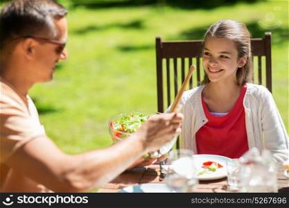 leisure, family, holidays and people concept - happy girl with father having festive dinner or summer garden party. happy girl with father eating at summer garden