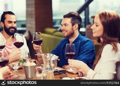 leisure, food and drinks, celebration people and holidays concept - smiling friends having dinner and drinking red wine at restaurant. friends dining and drinking wine at restaurant