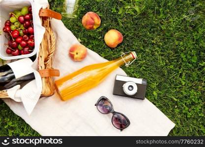 leisure, food and drinks concept - close up of picnic basket, bottle of fruit juice with sunglasses and film camera on grass. picnic basket, juice bottle, sunglasses and camera