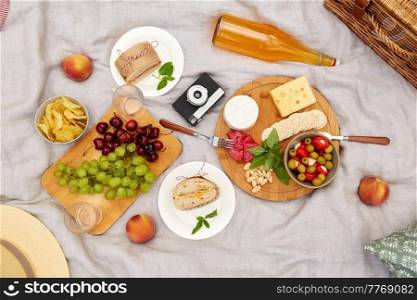 leisure, food and drinks concept - close up of snacks and camera on picnic blanket on blanket. food, drinks and picnic basket on blanket on grass