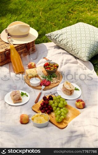 leisure, food and drinks concept - close up of snacks and picnic basket on blanket on grass at summer park. food, drinks and picnic basket on blanket on grass