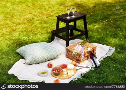 leisure, food and drinks concept - close up of snacks, wine and picnic basket on blanket on grass. food, drinks and picnic basket on blanket on grass