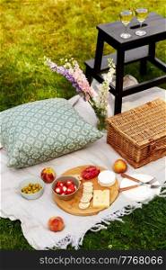 leisure, food and drinks concept - close up of snacks, wine and picnic basket on blanket on grass. food, drinks and picnic basket on blanket on grass