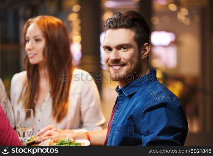 leisure, food and drinks, people and holidays concept - happy man with friends having dinner at restaurant