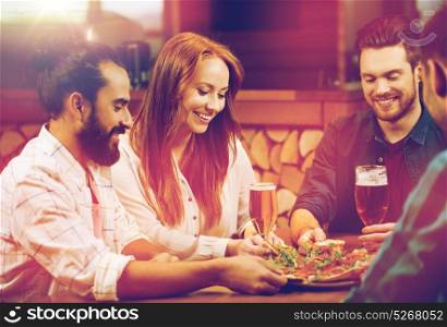 leisure, food and drinks, people and holidays concept - smiling friends eating pizza and drinking beer at restaurant or pizzeria. friends sharing pizza with beer at pizzeria