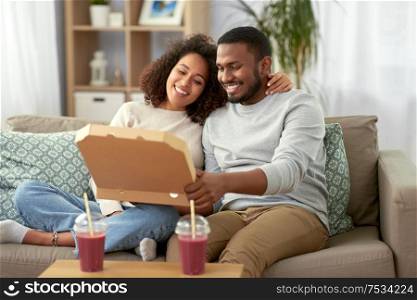 leisure, food and eating concept - happy african american couple with takeaway pizza at home. happy african american couple eating pizza at home