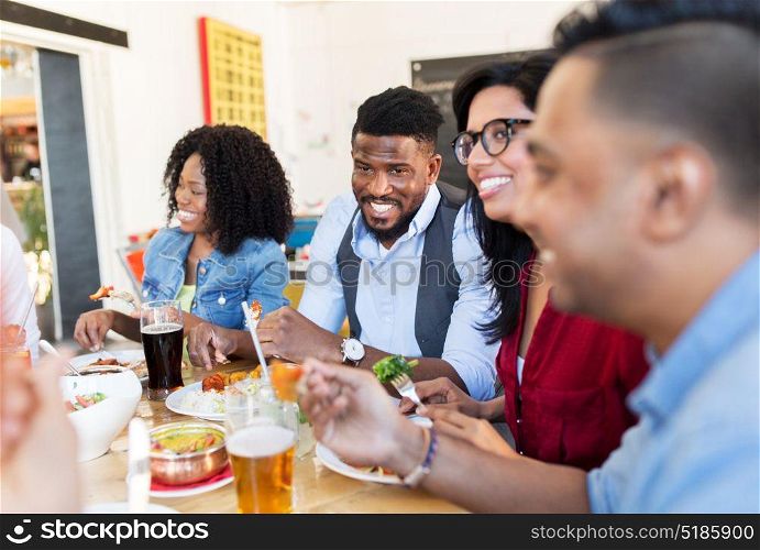 leisure, food and people concept - group of happy international friends eating and talking at restaurant table. happy friends eating and talking at restaurant