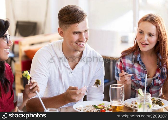 leisure, food and people concept - group of happy international friends eating and talking at restaurant table. happy friends eating and talking at restaurant